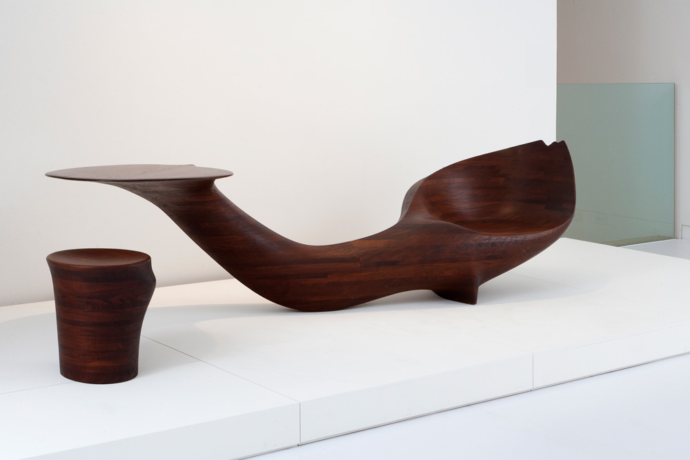 Table-Chair-Stool, 1968: (Installation view, The Aldrich Contemporary Art Museum, Wendell Castle-Wandering Forms-Works from 1959-1979, October 19, 2012-February 24, 2013)<br> Afromosia, African hardwoods<br> Table-Chair: 26-3/4 x 115-3/4 x 35 in. (67.9 x 294 x 88.9 cm); Stool: 16-5/8 x 16-1/4 x 14-5/8 in. (42.2 x 41.3 x 37.1 cm)<br> Museum of Arts and Design, gift of the Johnson Wax Company, through the American Craft Council, 1977<br> Photo courtesy of The Aldrich Contemporary Art Museum; Photo by Sherry Griffin/R & Company; © Wendell Castle, Inc.